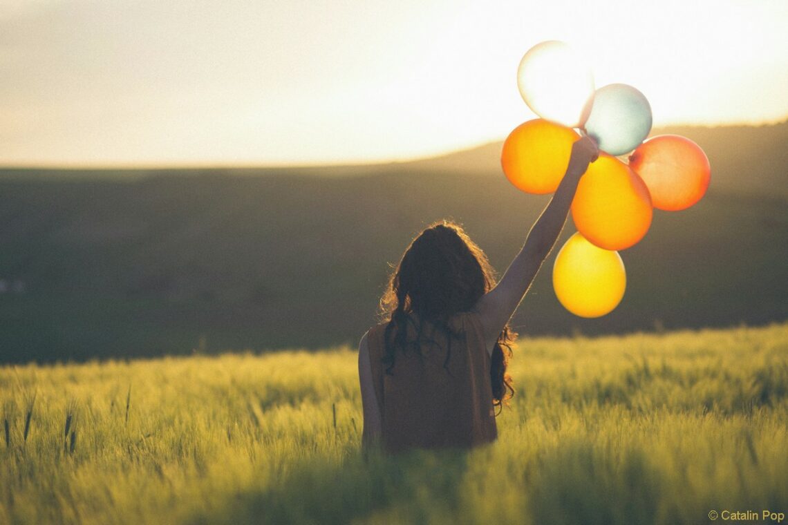 femme de dos brandit des ballons dans un champ