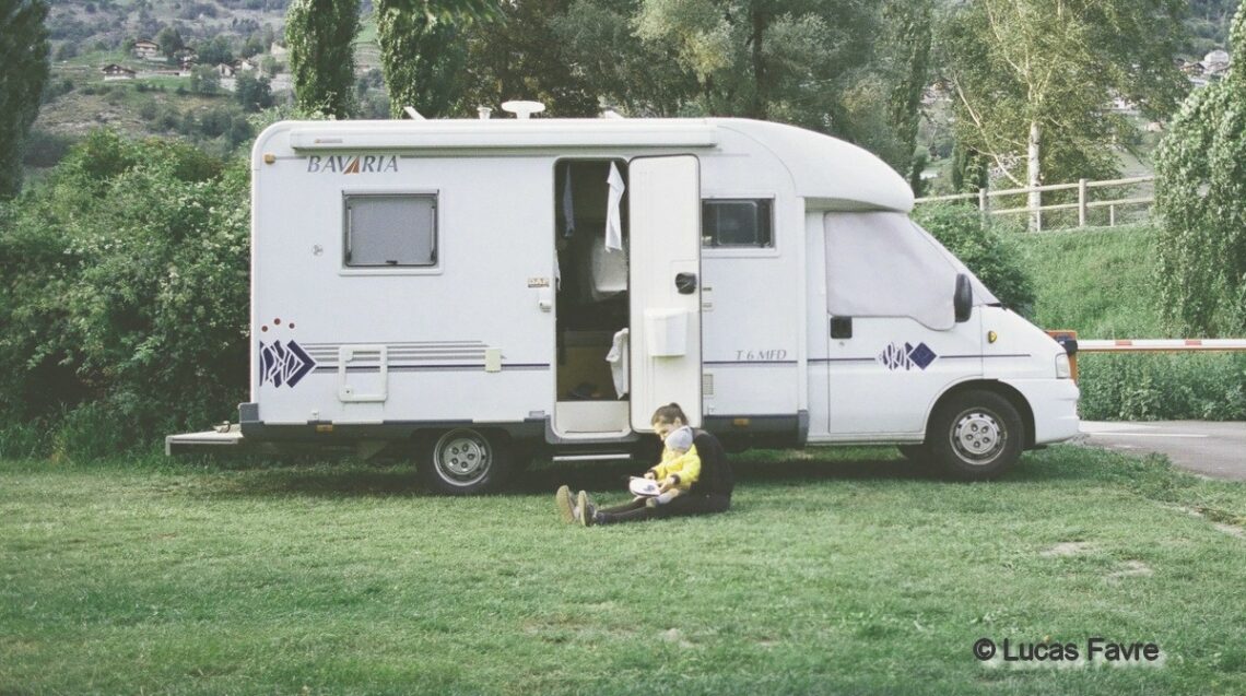 assise au pied de son camping-car, une maman tient son bébé sur elle