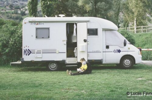 assise au pied de son camping-car, une maman tient son bébé sur elle