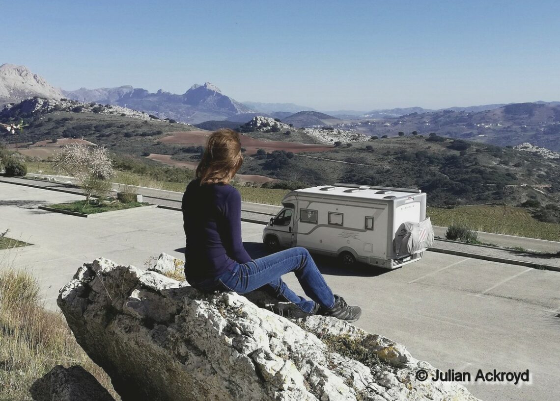 femme assise sur rocher contemple un camping-car en contrebas