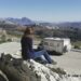 femme assise sur rocher contemple un camping-car en contrebas