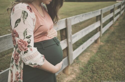 femme enceinte dans un pré, devant une barrière