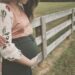 femme enceinte dans un pré, devant une barrière