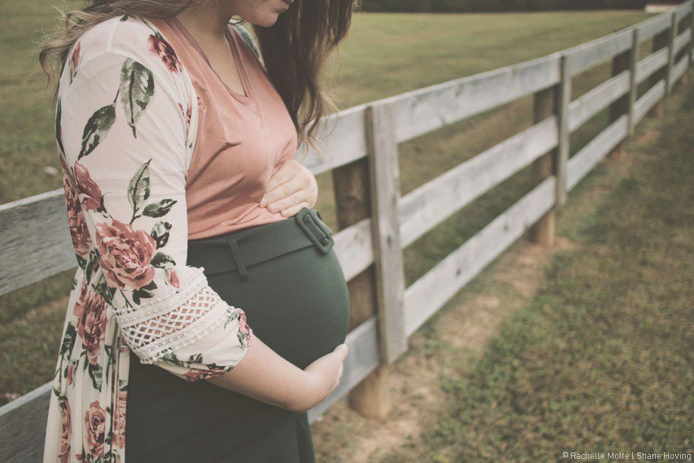 femme enceinte dans un pré, devant une barrière