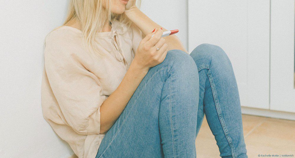 femme assise au sol, un test de grossesse dans la main