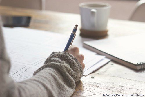image symbolisant la réflexion : une main tient un stylo au dessus d'une feuille, une tasse et un cahier