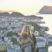 maman avec un bébé en porte-bébé devant un paysage d'un bord de mer avec soleil couchant