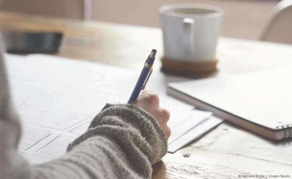 une main tient un stylo et écrit dans un journal
